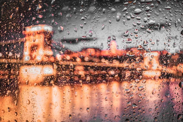 Night city lights through window with rainwater and drops. Background with bokeh.