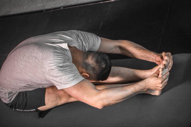 Yoga minderinin üzerinde beton duvara yaslanan genç bir adam. Beyaz tenli sporcu, güçlü kaslı vücut ve moda spor kıyafetleri yoğun antrenmandan önce ısınıyor..