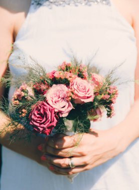 Gelin elinde güllerden bir buket tutuyor, düğün çiçekleri. Güzel bohem düğün çiçeği buketi. Bir buket gülü elbisesi olan kız..