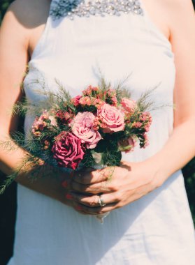 Gelin elinde güllerden bir buket tutuyor, düğün çiçekleri. Güzel bohem düğün çiçeği buketi. Bir buket gülü elbisesi olan kız..