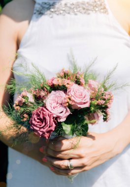 Gelin elinde güllerden bir buket tutuyor, düğün çiçekleri. Güzel bohem düğün çiçeği buketi. Bir buket gülü elbisesi olan kız..