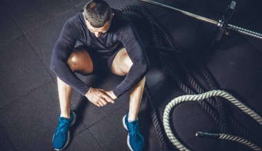 Eğitimden sonra dinleniyorum. Spor salonundaki paspasın üzerinde oturan sakallı genç adamın bakışları. Yüksek resulotion resmi.