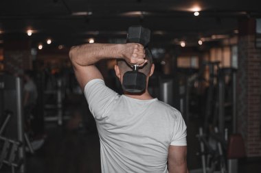 Delikanlı vücut geliştirici koyu renk spor salonunda halterle egzersiz yapıyor..