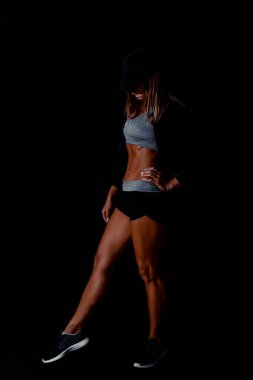 Stüdyoda poz veren atletik bir kadın, vücut geliştirici. Kaslı seksi vücut ve güçlü kaslar. Siyah arka planda çekilmiş, gösterişsiz. Vücut geliştirme kavramı.