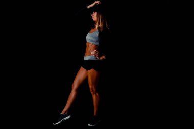 Siyah bir arka planda sırtını esneten çekici bir kadın. Eğitiminden sonra terden sırılsıklam olmuş halde karanlık bir stüdyoda seksi fitness modeli..