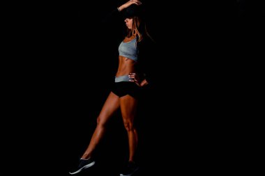 Siyah bir arka planda sırtını esneten çekici bir kadın. Eğitiminden sonra terden sırılsıklam olmuş halde karanlık bir stüdyoda seksi fitness modeli..