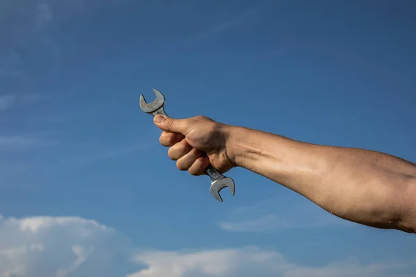 Hand with a wrench on a background of the sparkling blue sky.