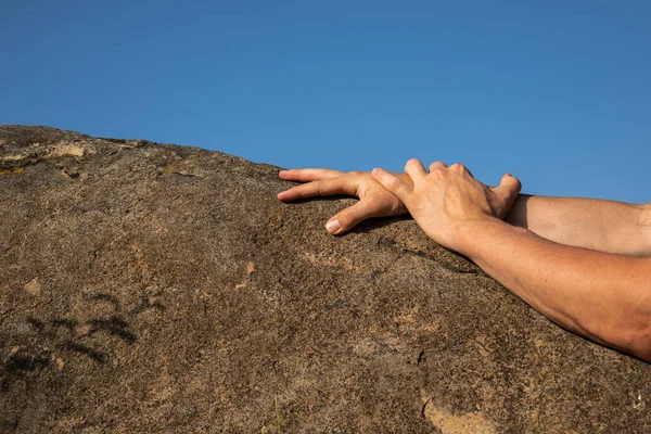 Rock climber\'s hands on handhold on blue sky background.