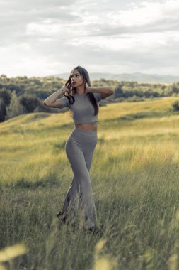Doğanın tadını çıkaran güzel bir kız. Minimalist tarzda gri elbiseli güzel bir manken yaz sahasında poz veriyor, güneş ışığı. Sahadaki romantik esmer kız. Şehvetli, sakin kız, gün batımı.