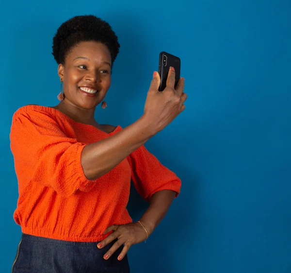 black woman smiling looking at a cellphone in her hands  on studio with a blue blackground