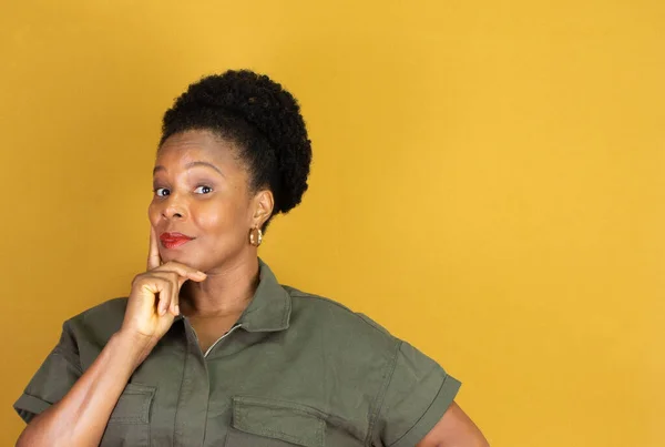 black woman smiling in a green outfit and thinking on a yellow background