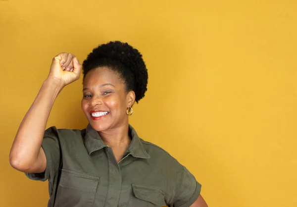 black woman in green clothes making victory gesture on a yellow background