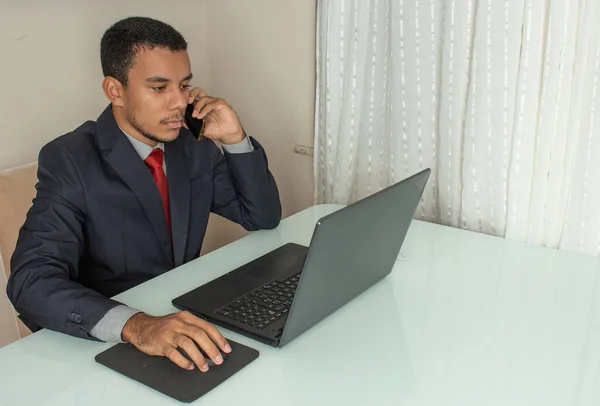 executive man looking at a computer and holding a  cellphone  and a mouse at the same time with a cup of cofee under the white table at the office