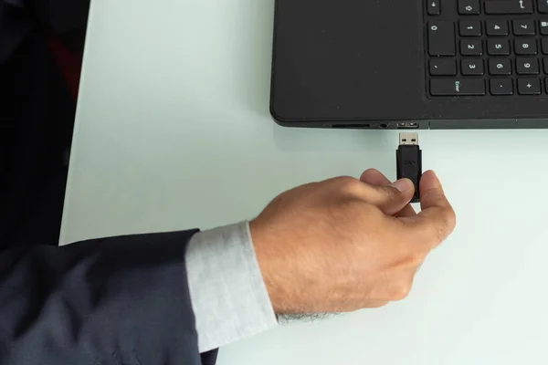 executive man holdind a pen drive and trying to insert in a computer under the white table