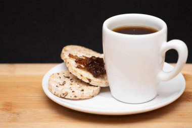 a cup of coffe beside a  rice vegan cookies with jelly on the top