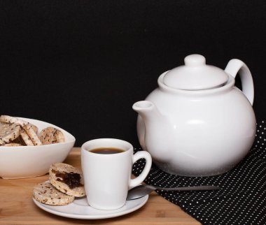a cup of coffee surrouded  a  bowl full of  rice vegan cookies and a coffe pot