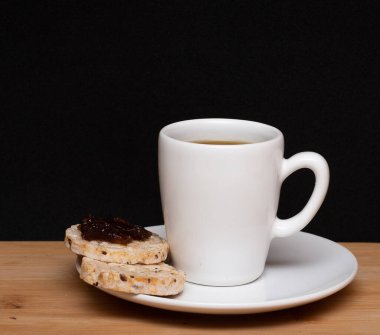 cup of coffe beside a rice vegan cookies with jelly on the top under the wood table