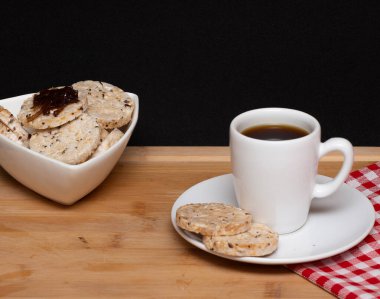 a cup of coffe beside a  rice vegan cookies with jelly on the top  and a bowl full of rice cookies