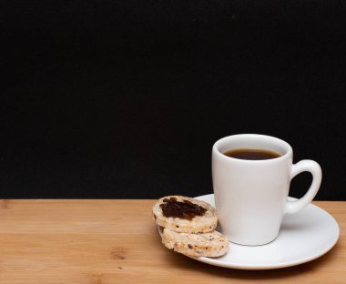 cup of coffe beside a rice vegan cookies with jelly on the top under the wood table