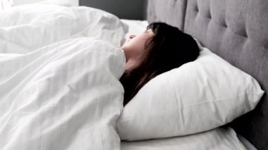 Genç beyaz kadın uyuyamıyor, battaniyenin altında yatıyor. Yatakta uykusuzluk ve baş ağrısı çekiyor. Huzursuz kız yorgun ve uykulu. Evdeki yatak odasında yastıkla kaplanmış..