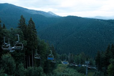 Bukovel, Ukrayna - Temmuz 2020: Kayak asansörü yaz mevsiminde Karpat dağlarında yukarı doğru hareket ediyor. Ukrayna 'da yaz tatili. Tepede bir asansörle turist taşımacılığı. Güzel orman manzarası