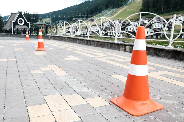 Orange striped road cones on a pavement. Safety equipment for traffic on a street, car barricade equipment for driving lessons. Plastic security cone for caution, sign to be careful behind the wheel.