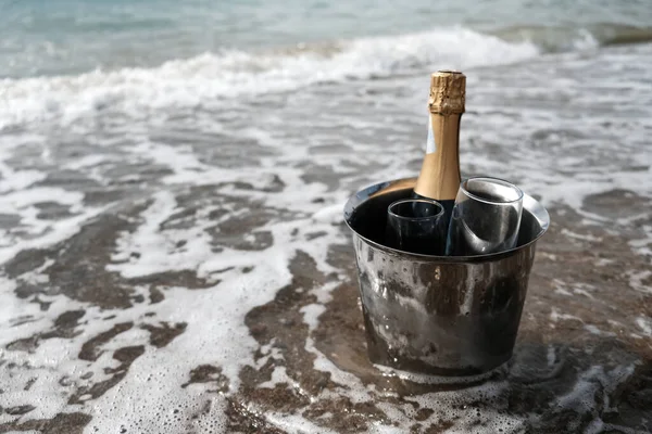 Ice bucket with champagne bottle and glasses on a beach surrounded by sea. Ocean waves chilling drinks, luxury vacation for two. Anniversary day, romantic holiday or honeymoon together. Tourist couple