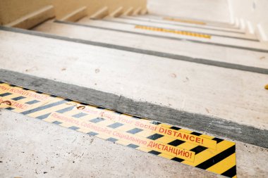 Lütfen sosyal mesafeni koru! Coronavirus sırasında merdivenlerde uyarı. Dünya çapında küresel salgın güvenlik önlemleri. Parlak sarı ve siyah ile mesafelendirme için çok dilli mesaj