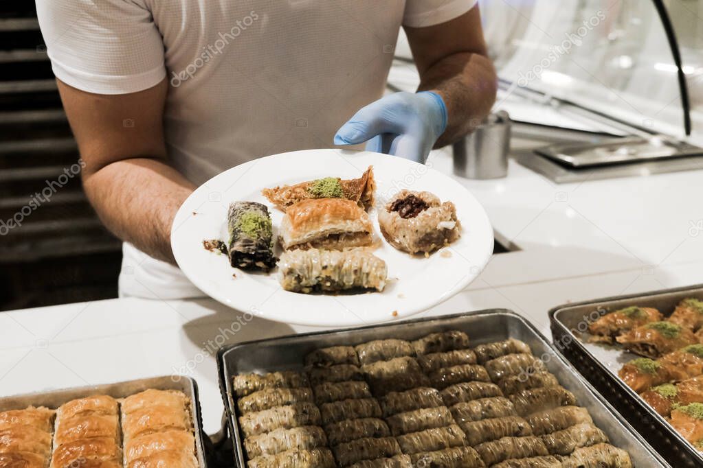 Staff in gloves giving Turkish baklava to a tourist at all-inclusive hotel in Turkey. Delicious traditional sweets on a plate. Assortment of eastern treats for lunch at a luxury resort in Antalya.