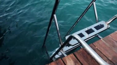 Overview of the beach from the dock near a staircase. Deep sea water with waves and tourists chilling at the beach. Sunny day near the ocean. Preparing for the first scuba diving lesson overseas.