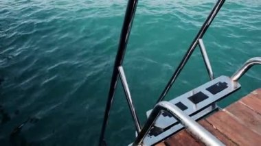 Closeup view of the dock with staircase down into the deep blue sea water. Beautiful ocean is perfect for scuba diving, swimming or snorkeling as a tourist on vacation. Waves from windy weather.