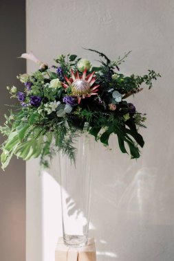 Kral protea çiçeği, lahana gülleri, canavar yaprakları ve cam bir vazoda diğer yeşilliklerle birlikte modaya uygun ve egzotik bir çiçek tasarımı. Lüks bir düğün ya da şık bir etkinlik için modern bir buket taze çiçek..