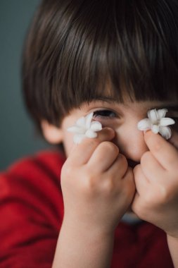 Sevimli oyuncu çocuk gözlerini beyaz bahar çiçeğiyle kaplıyor. Otantik mutlu çocuk oyunu.  