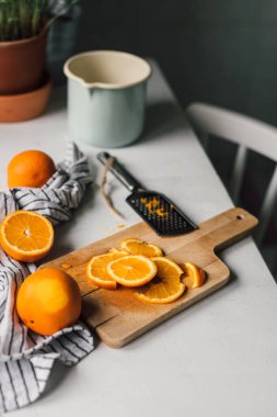 Ahşap tahta, bez, rende ve meyve suyu bardağıyla dilimlenmiş portakallar kırsal mutfak içinde beyaz masanın üzerinde. Ev yaşamında yemek pişirmek. 