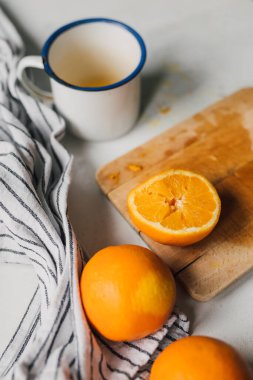 Yarısı ahşap tahta tahtada, yarısı retro emaye bardakta taze sıkılmış, organik portakallar ve beyaz masada mutfak örtüsü. Turunçgillerden meyve suyu yapıyorum. Sağlıklı diyet yaşam tarzı. Seçici odak.