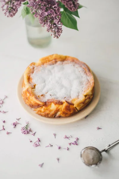 新鲜烘焙的番茄酱芝士蛋糕放在白桌上 玻璃花瓶里放着紫丁香花 自制的带有有机成分的乡村蛋糕 无肉派加奶酪和浆果食品风格 有选择的重点 图库图片