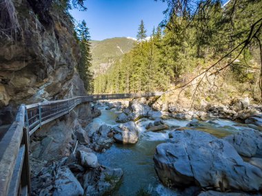 Alplerdeki hızlı dağ nehri üzerinde köprüsü olan ahşap yol.