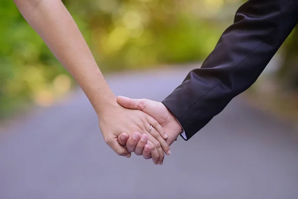 A married couple holding hands with the road in the background.