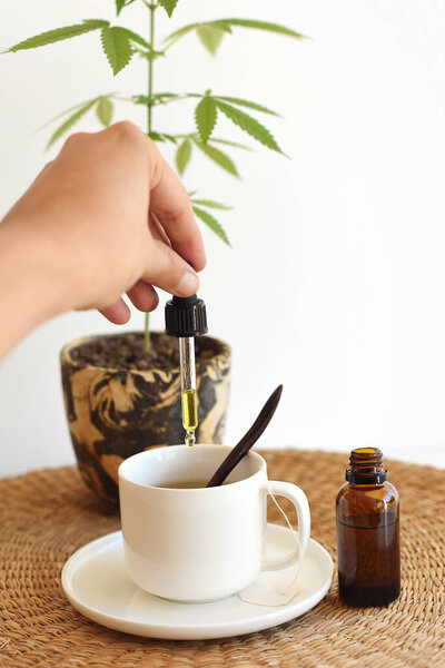 Hand pouring drops of CBD oil in the infusion cup, medical cannabis concept 