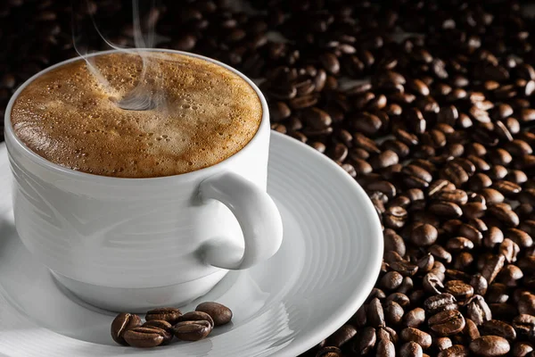 a cup of fresh, brewed coffee standing on a saucer in which several coffee beans lie. steam hovers over the drink. scattered coffee beans serve as background.