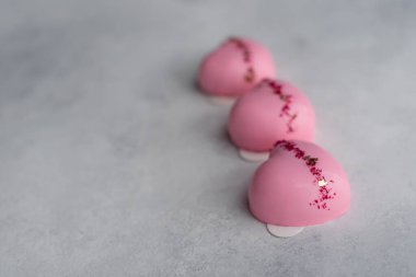Altın yaprak ve gri taştan arka planda kurumuş gül yapraklarıyla süslenmiş aynalı jöleli üç kalp şeklinde pembe kek. Sevgililer Günü için gurme Fransız pastaları, kopyalama macunu, metin için yer