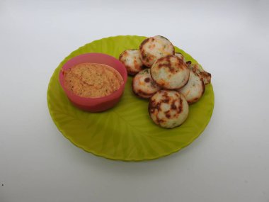 Paddu ya da Kuzhi Paniyaram ve Hindistancevizli Chutney 'nin Beyaz Arkaplan' da izole edilmiş yeşil tabakta yakın çekimi. Küf kullanarak hamuru buharla pişirilen Hint yemeği. Hamur siyah mercimek ve pirinçten yapılmıştır..