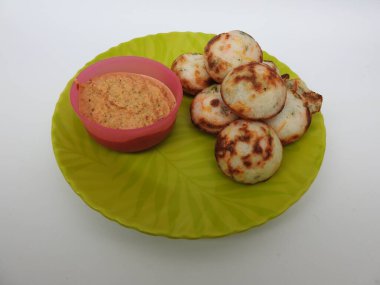 Paddu ya da Kuzhi Paniyaram ve Hindistancevizli Chutney 'nin Beyaz Arkaplan' da izole edilmiş yeşil tabakta yakın çekimi. Küf kullanarak hamuru buharla pişirilen Hint yemeği. Hamur siyah mercimek ve pirinçten yapılmıştır..