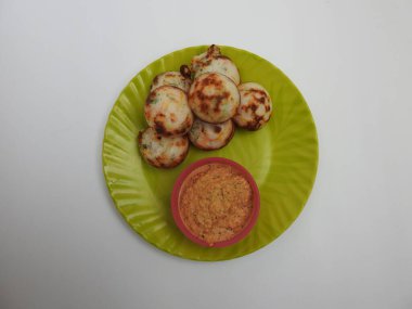 Paddu ya da Kuzhi Paniyaram ve Hindistancevizli Chutney 'nin Beyaz Arkaplan' da izole edilmiş yeşil tabakta yakın çekimi. Küf kullanarak hamuru buharla pişirilen Hint yemeği. Hamur siyah mercimek ve pirinçten yapılmıştır..