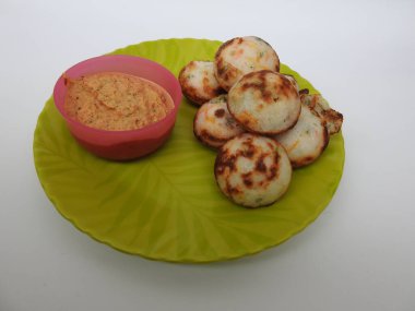 Paddu ya da Kuzhi Paniyaram ve Hindistancevizli Chutney 'nin Beyaz Arkaplan' da izole edilmiş yeşil tabakta yakın çekimi. Küf kullanarak hamuru buharla pişirilen Hint yemeği. Hamur siyah mercimek ve pirinçten yapılmıştır..