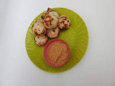 Paddu ya da Kuzhi Paniyaram ve Hindistancevizli Chutney 'nin Beyaz Arkaplan' da izole edilmiş yeşil tabakta yakın çekimi. Küf kullanarak hamuru buharla pişirilen Hint yemeği. Hamur siyah mercimek ve pirinçten yapılmıştır..