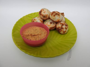 Paddu ya da Kuzhi Paniyaram ve Hindistancevizli Chutney 'nin Beyaz Arkaplan' da izole edilmiş yeşil tabakta yakın çekimi. Küf kullanarak hamuru buharla pişirilen Hint yemeği. Hamur siyah mercimek ve pirinçten yapılmıştır..