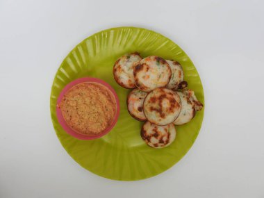 Paddu ya da Kuzhi Paniyaram ve Hindistancevizli Chutney 'nin Beyaz Arkaplan' da izole edilmiş yeşil tabakta yakın çekimi. Küf kullanarak hamuru buharla pişirilen Hint yemeği. Hamur siyah mercimek ve pirinçten yapılmıştır..
