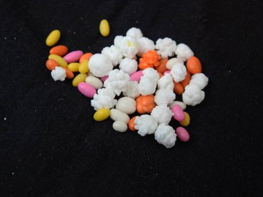 Siyah arkaplana saçılmış renkli şeker kaplı beyaz toplar ve rezene tohumları..