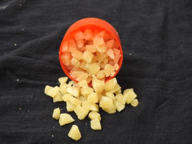 Sarı renkli Jaggery Dilimlerinin yakın plan resmi veya siyah arka planda izole edilmiş Plastik bardak ve kum kabındaki Parçalar